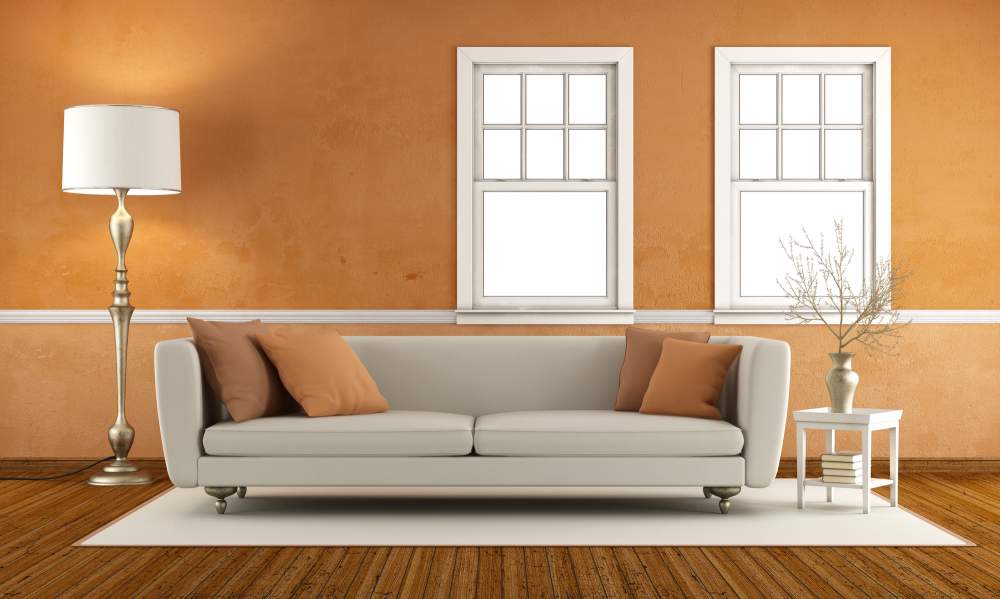 An orange wall with two windows over a couch