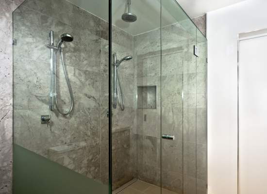 Glass enclosed shower with marble walls